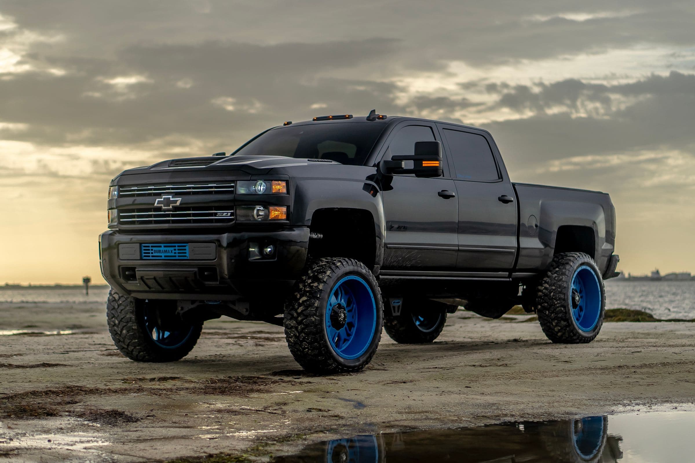 Lifted, blacked-out Chevy Silverado on custom wheels at sunset